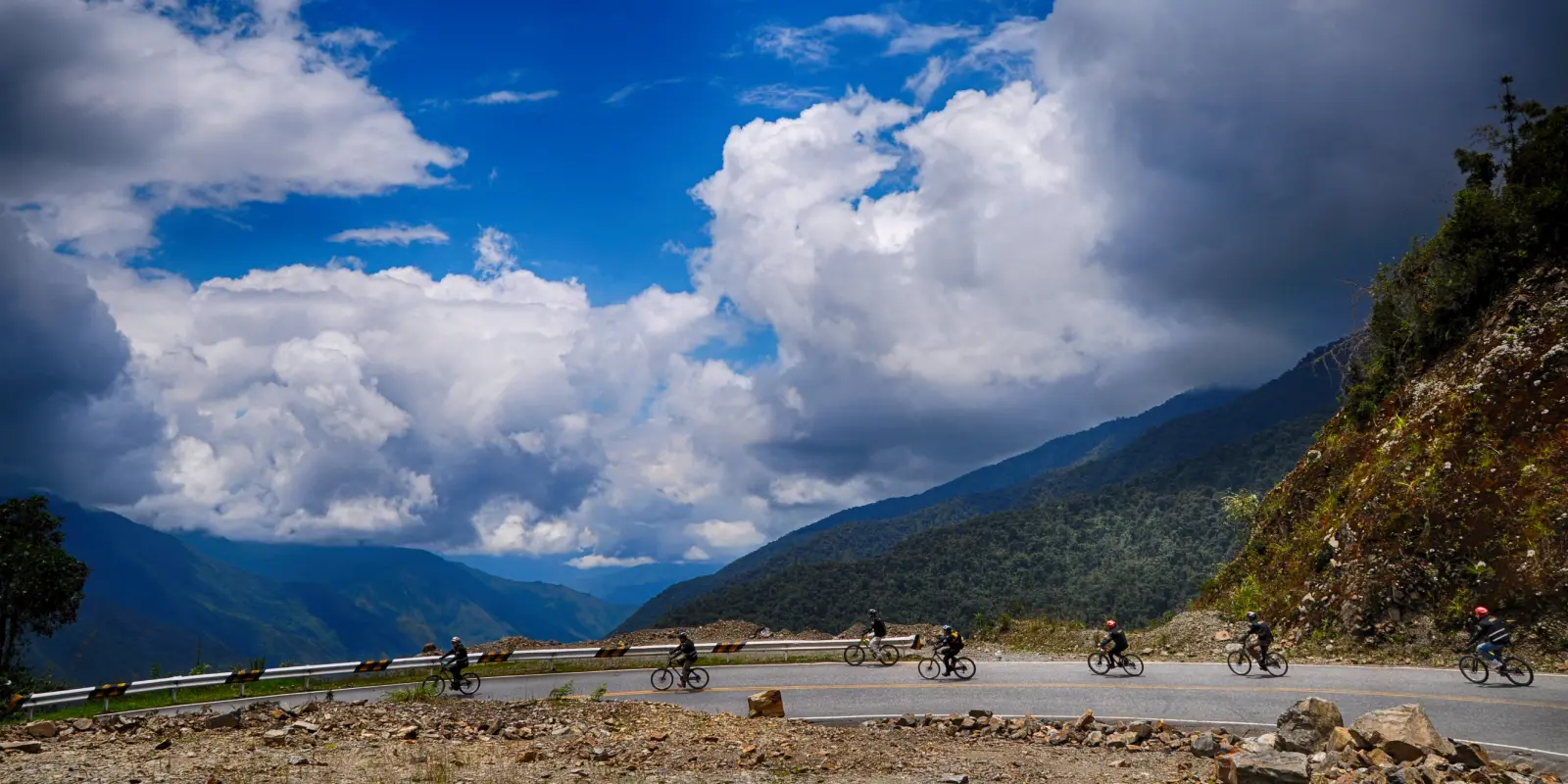Ciclistas descendiendo por el camino de Abra Malaga en el tour Inca Jungle. Vista panorámica de montañas verdes y cielo azul con nubes, ruta emblemática hacia Machu Picchu en Perú