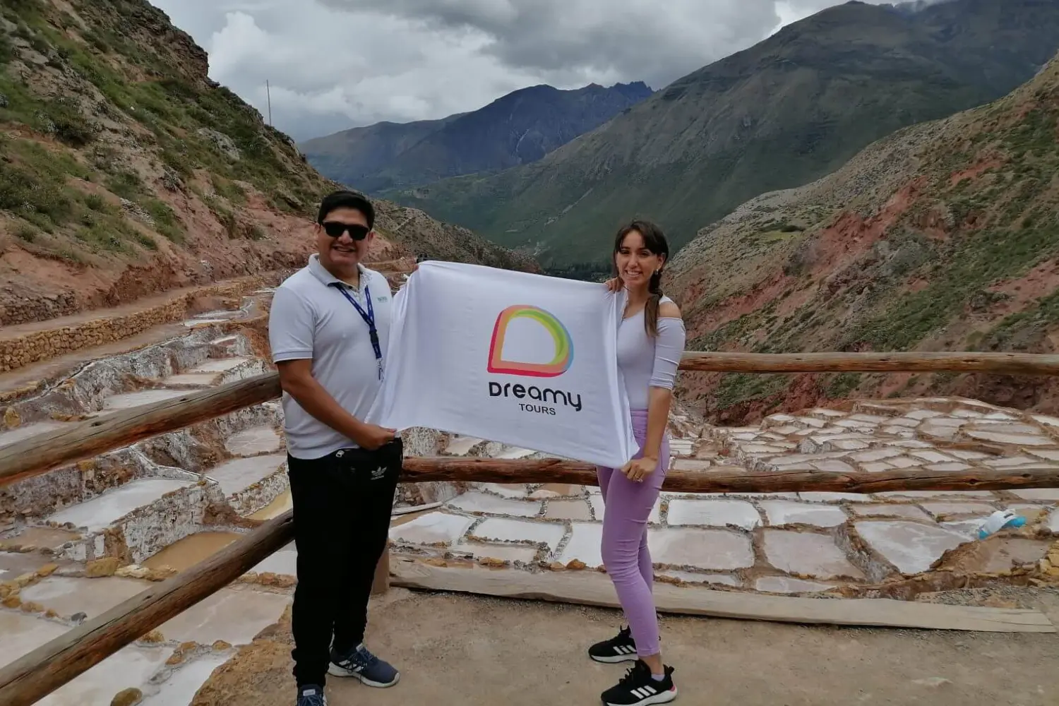 Casal feliz nas salinas de Maras com a bandeira da Dreamy Tours.